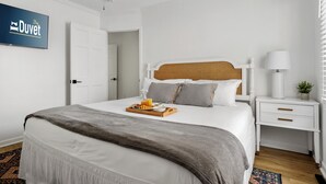 Une chambre d’hôtel bien rangée, avec un lit, une table de chevet et un téléviseur fixé au mur.