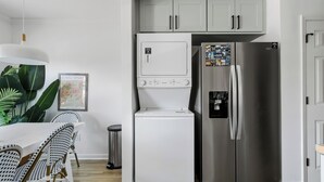 Une cuisine avec un réfrigérateur blanc, un lave-linge blanc et un réfrigérateur-congélateur en acier inoxydable. On y trouve une table à manger avec des chaises et un luminaire suspendu.