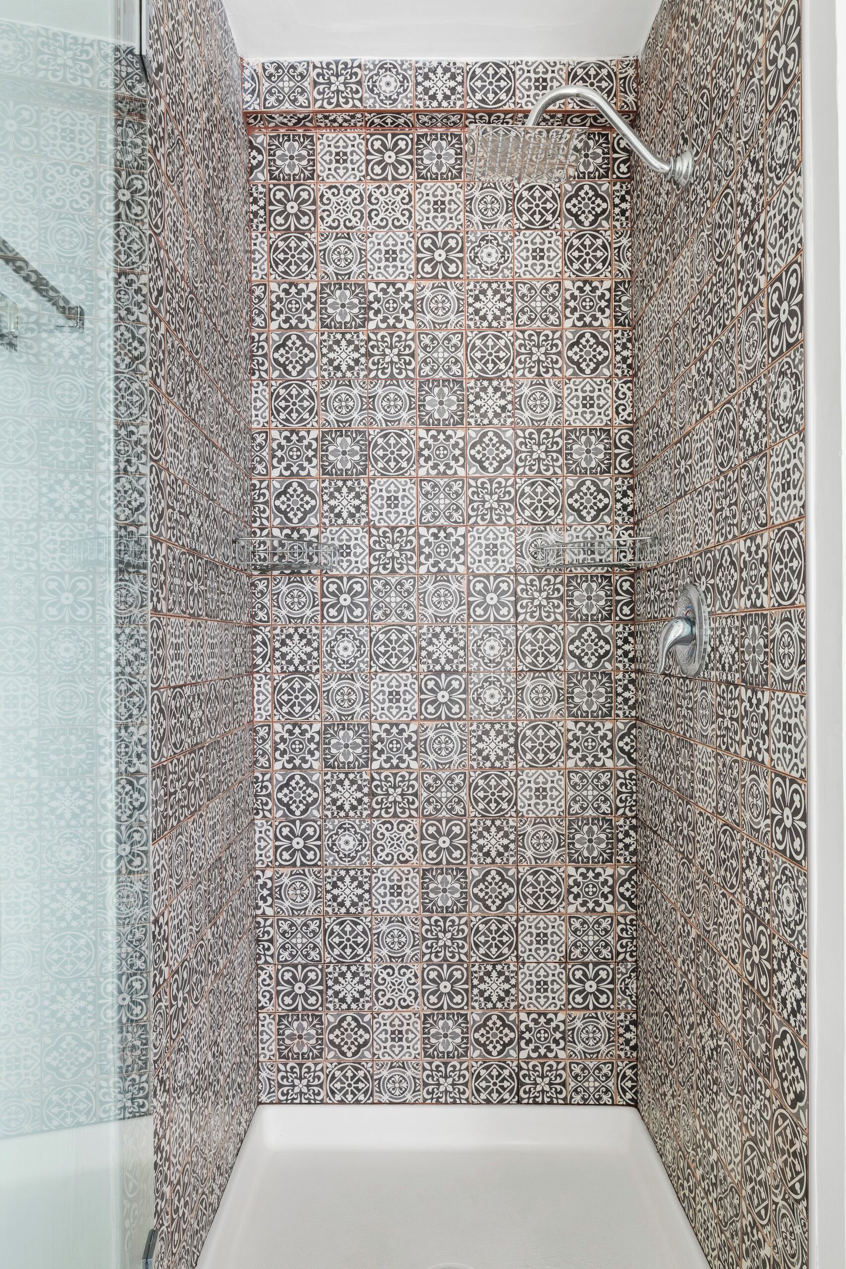 Ducha con intrincados diseños de azulejos y cabezal de ducha de mano.