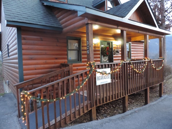 A log cabin with a porch decorated with lights and a sign reading "BEARADISE".