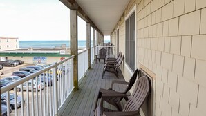 A covered outdoor area with wooden flooring and beige walls, featuring several chairs and a railing. - Grand Victorian on the Beach, Summer (Old Orchard Beach)