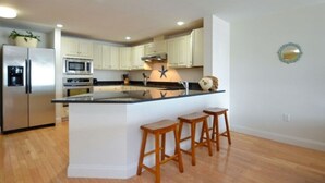 A modern kitchen with white cabinets, stainless steel appliances, and a central island with stools. - Grand Victorian on the Beach, Summer (Old Orchard Beach)