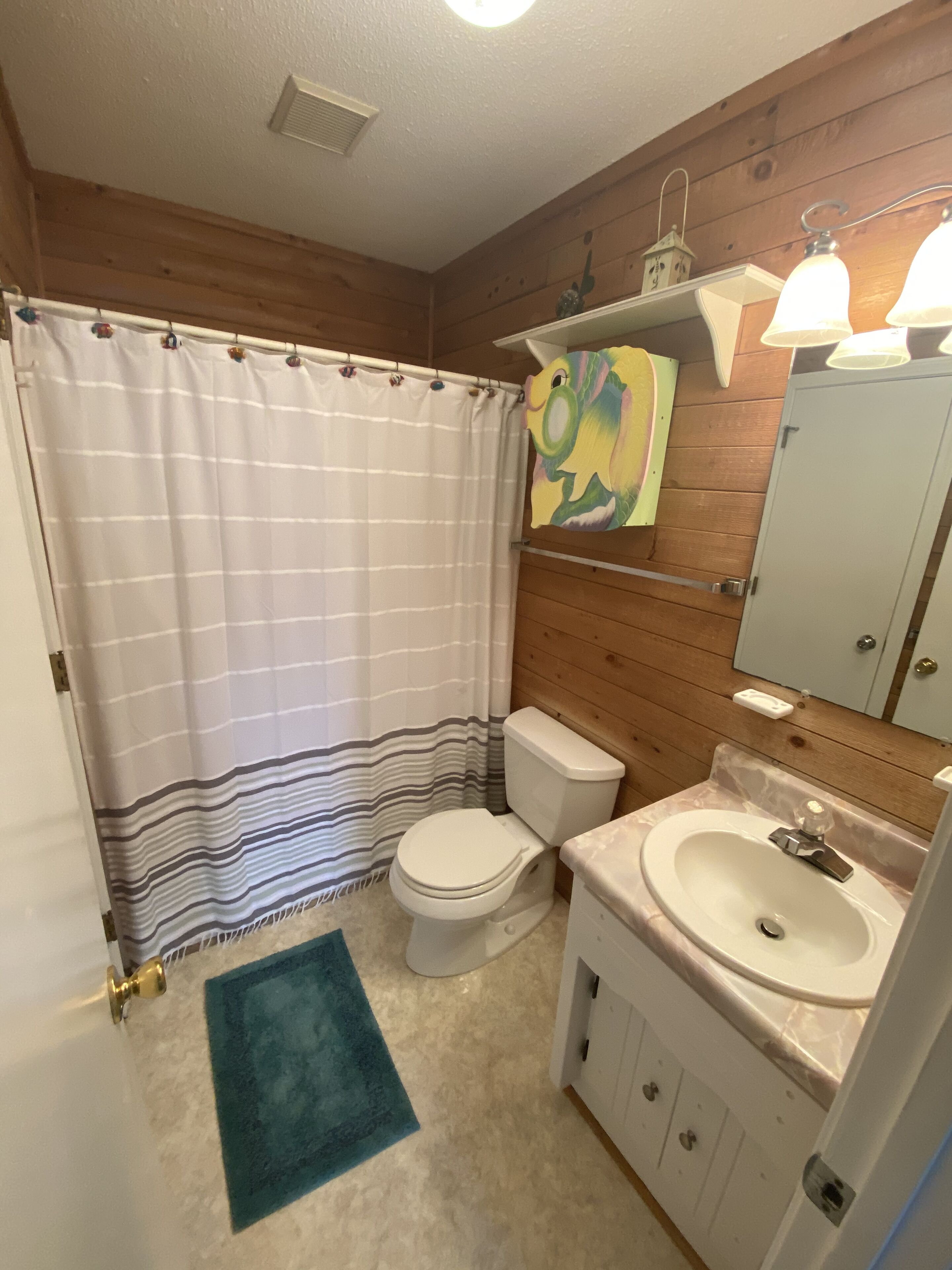 Un bagno con una tenda da doccia a righe, un water, un lavandino e una parete in legno.