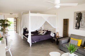 A bedroom with a four-poster bed, a grey sofa, a small table, and a potted plant.