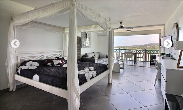 A four-poster bed with a canopy, a balcony with a view, and a seating area with a table and chairs.