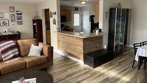 Un soggiorno moderno con un divano in pelle marrone, un tavolo da pranzo in legno e un angolo cottura con mobili in legno e un frigorifero nero.
