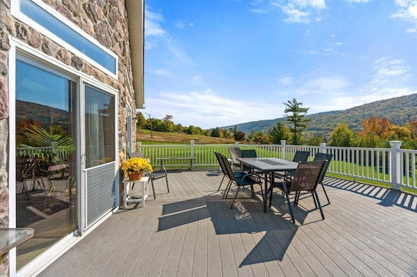 A deck with a table and chairs, overlooking a scenic landscape with hills and trees.