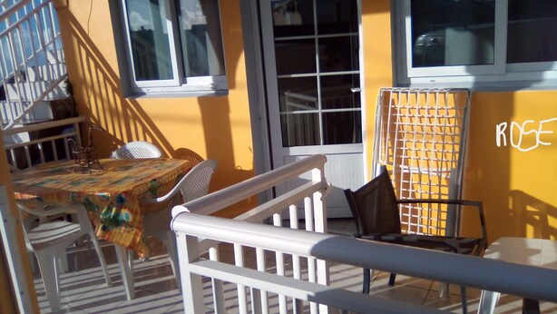 A balcony with a table and chairs, a staircase, and a window with a grid pattern. - APARTMENT LA DAME DE FER (GOSIER)