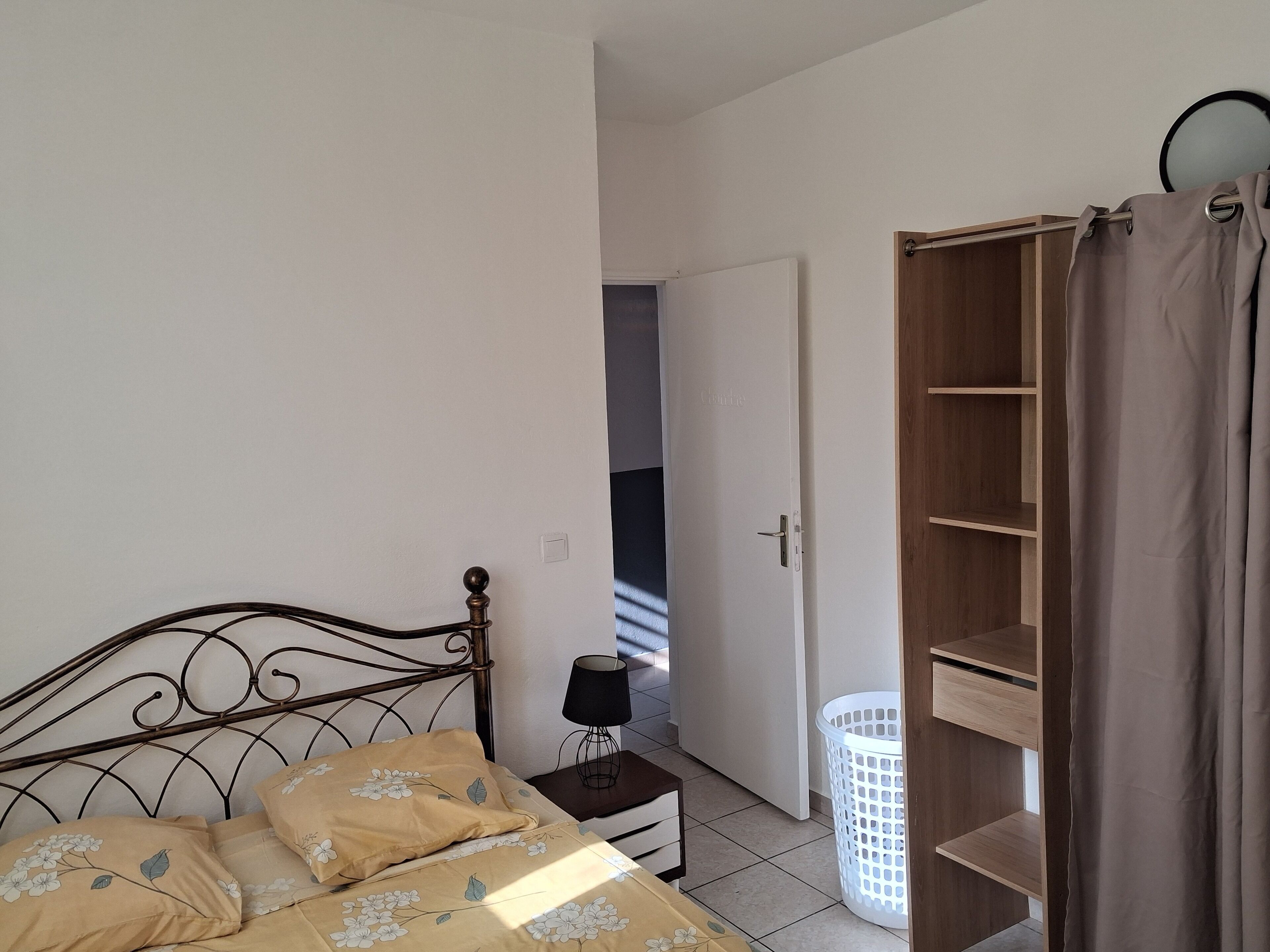 Ein Schlafzimmer mit einem Bett, einem Nachttisch, einem Kleiderschrank und einer Tür zu einem anderen Raum.