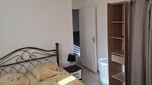 A bedroom with a bed, a nightstand, a wardrobe, and a door leading to another room. - APARTMENT LA DAME DE FER (GOSIER)