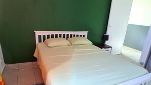 A room with a bed, a small bedside table, a green wall, and a door. - APARTMENT LA DAME DE FER (GOSIER)