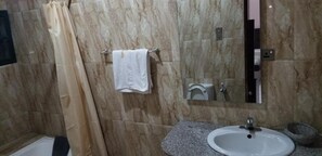 Une salle de bain avec un mur en marbre, un lavabo blanc, une serviette suspendue à un porte-serviettes et un rideau de douche.