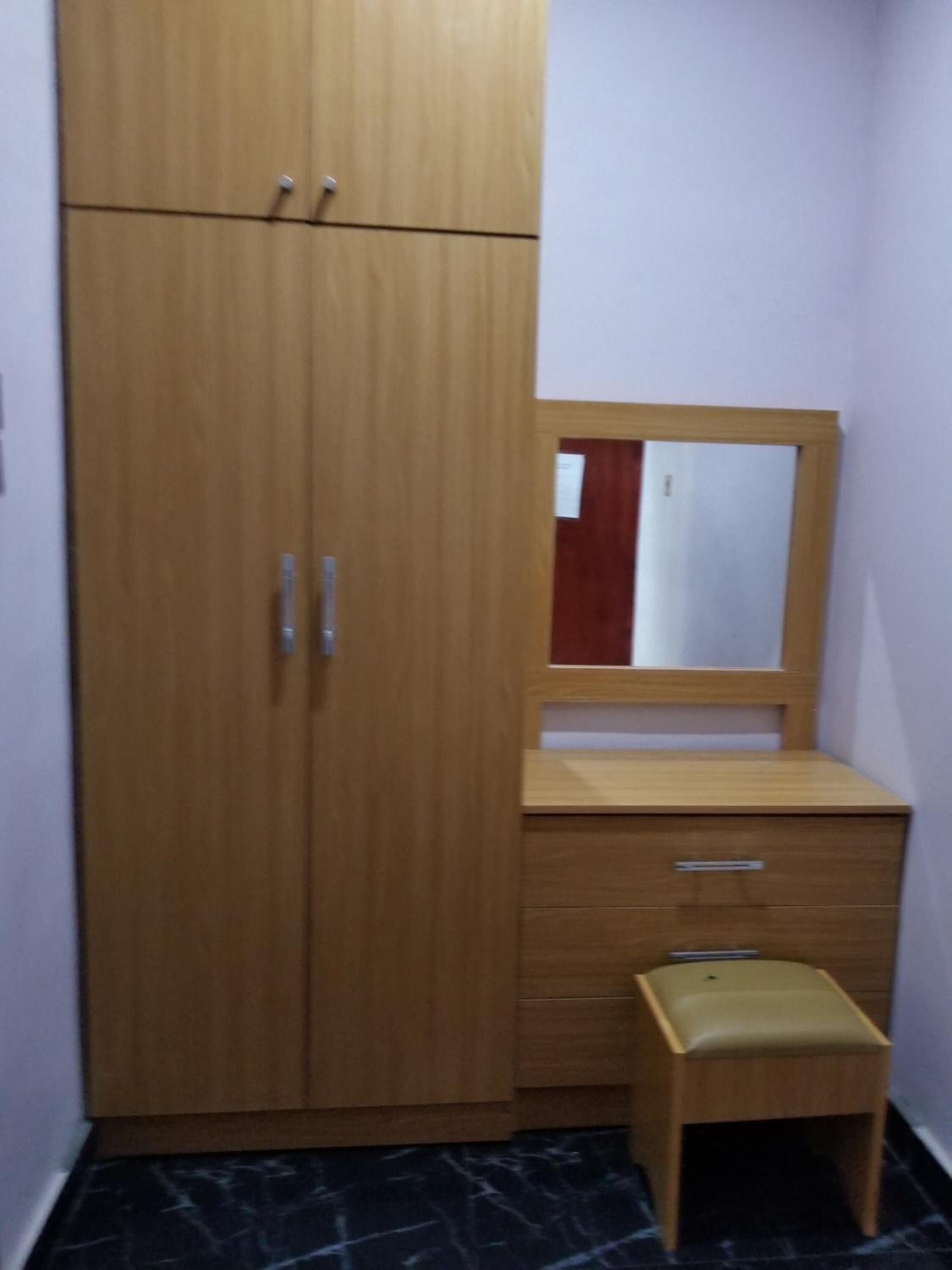 Une petite pièce avec une armoire en bois, un miroir, un petit tabouret et un sol en marbre.