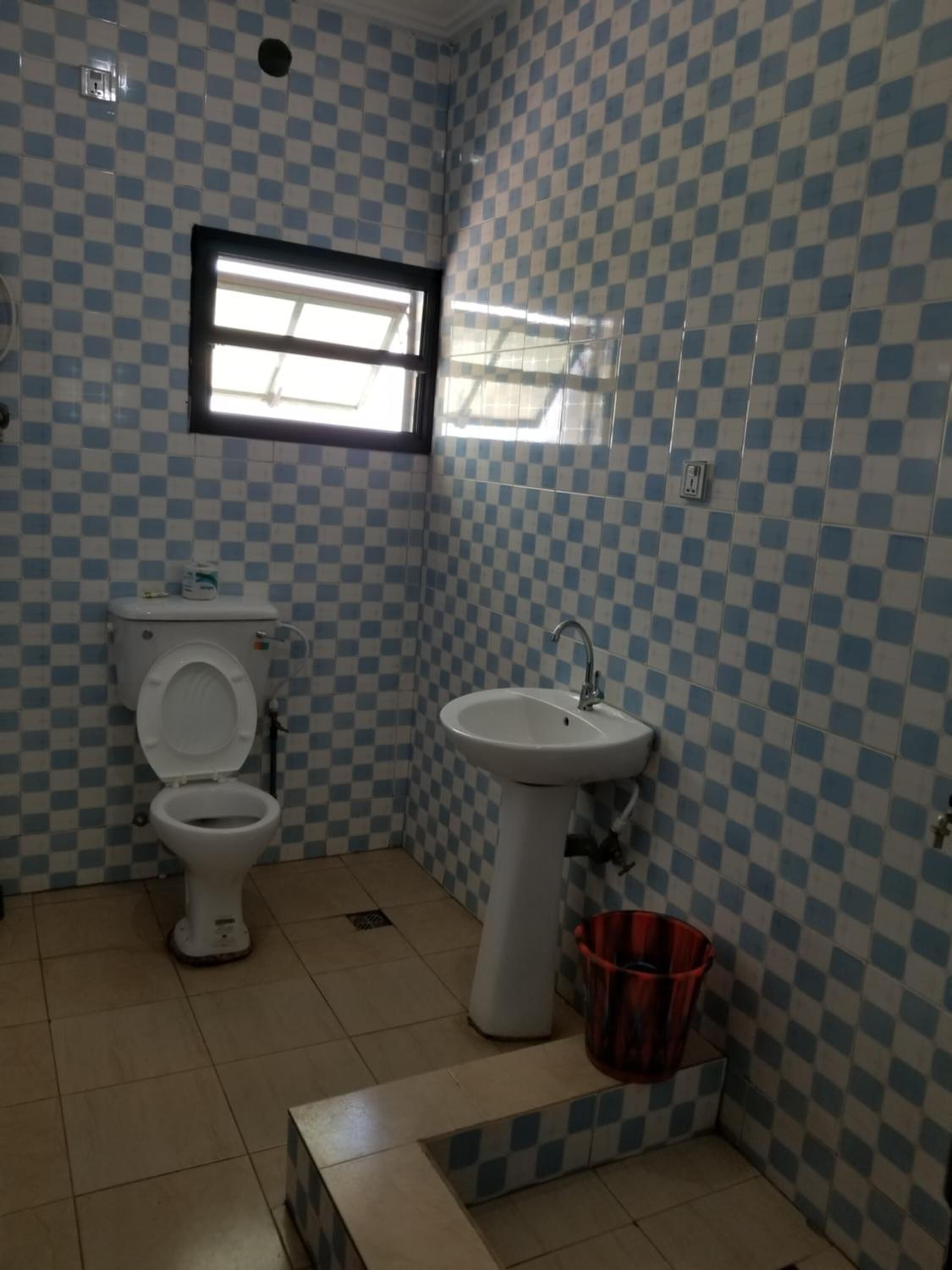 A bathroom with a checkered tile pattern, a toilet, a sink, and a window.