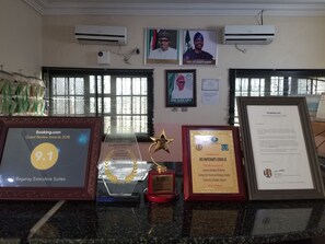 Un espace d’accueil d’hôtel agrémenté de trophées, de certificats et d’une photographie encadrée d’un homme.