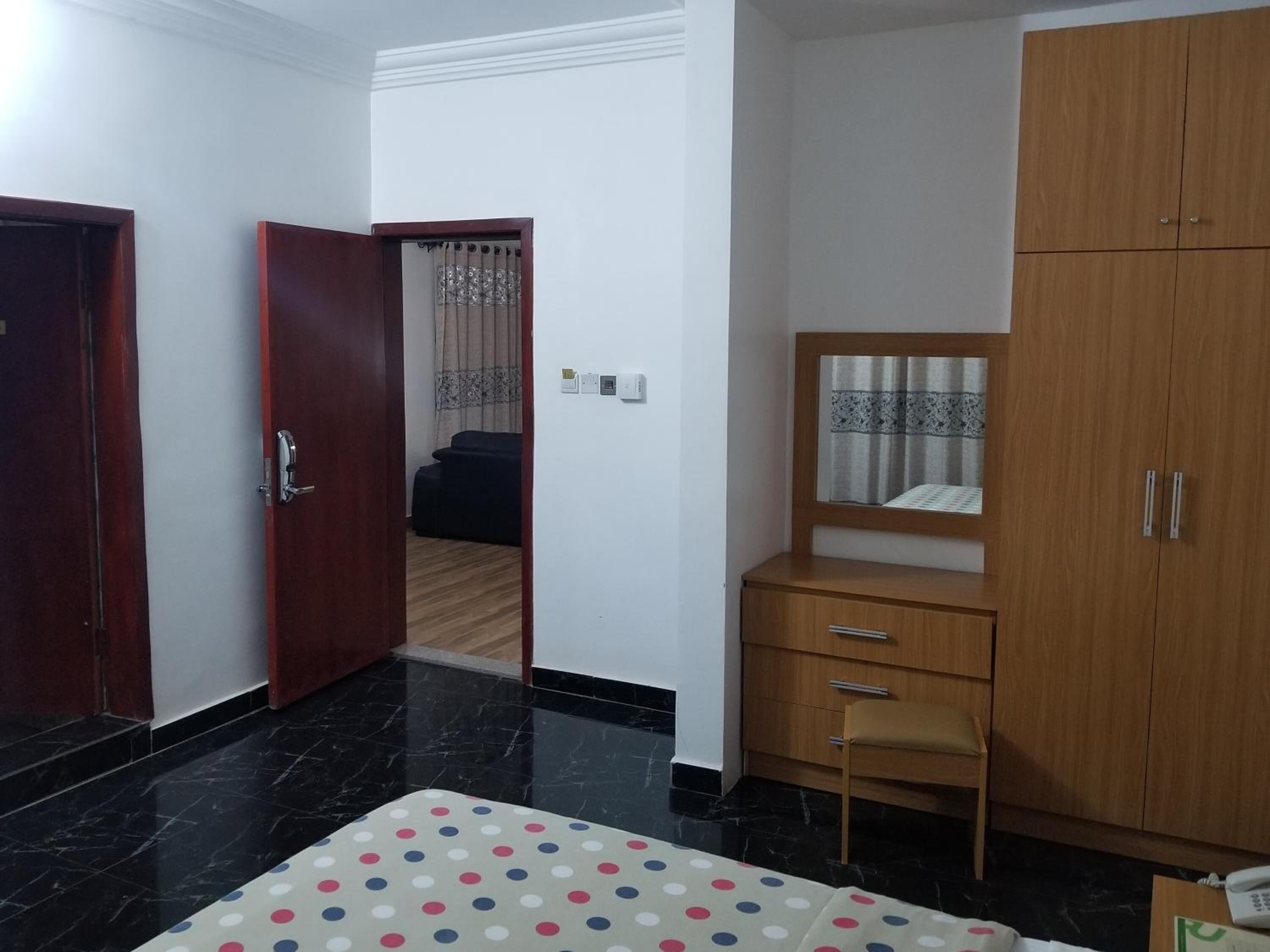A room with a wooden wardrobe, a small desk, a chair, and a polka dot tablecloth.