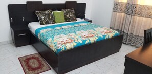 Un lit avec une couvre-lit à motifs floraux, une table de chevet, une commode et un tapis rouge.