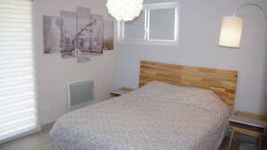 A bedroom with a wooden headboard, a bed with a patterned bedspread, a wall-mounted lamp, and artwork on the wall. - Bright cottage with terrace, garden and parking (Lédenon)