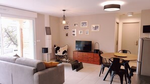 A modern living room with a grey sofa, a dining table with chairs, a TV, and a refrigerator. - Bright cottage with terrace, garden and parking (Lédenon)