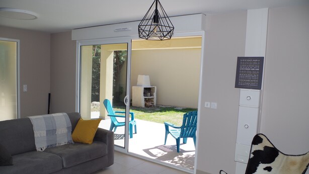 A modern living room with a grey sofa, a blue armchair, and a cowhide chair. A glass door leads to an outdoor area with a lawn and chairs. - Bright cottage with terrace, garden and parking (Lédenon)