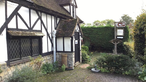 A traditional Tudor-style building with a cobblestone courtyard, a sign indicating a nearby location, and a small garden area.