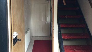 A hallway with a red carpet leading to a white door, a staircase with red steps, and a radiator on the wall.