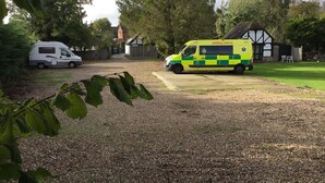 An ambulance parked in a driveway with a house in the background.