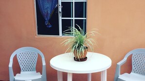 Une petite table ronde, deux chaises, une plante en pot et une fenêtre avec un rideau.
