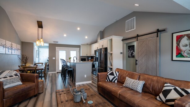 A modern living room with a brown leather sofa, a wooden coffee table, and a dining area with a kitchen in the background. - University Area Bungalow - The Moxie Harris House (Eugene)