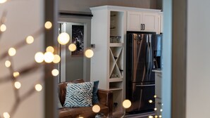 A modern kitchen with white cabinetry, a stainless steel refrigerator, and a dining area with a brown leather couch. - University Area Bungalow - The Moxie Harris House (Eugene)