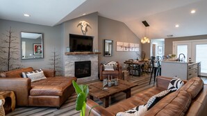 A modern living room with a fireplace, leather sofas, a dining area, and a kitchen. - University Area Bungalow - The Moxie Harris House (Eugene)