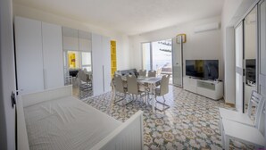 A modern, well-lit room with a bed, dining table, chairs, a TV, and a large window offering a view. - Villa Francesca Sicily 8, Apartment in Villa on the sea (casteldaccia)