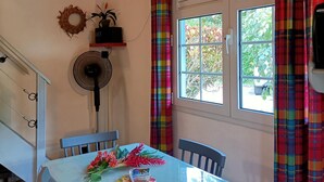 A dining area with a table, chairs, a fan, and a window with curtains. - COLIBRI BLE -villa at the seaside .................................... (Sainte-Anne)