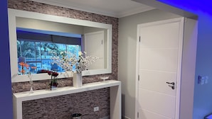 A modern interior with a stone wall, a white console table, a mirror, and a door. - High standard apt 200mts and sea view and complete recreation area (Guarujá)