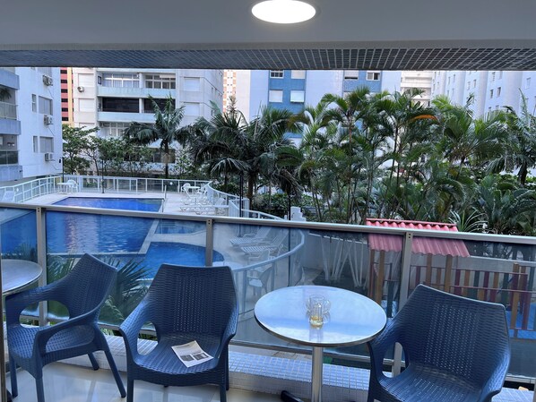 Un espace piscine aménagé sur le toit, avec des chaises longues et des tables, entouré de palmiers et d’immeubles.
