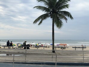 Een strand met palmbomen, parasols en mensen.