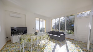 A spacious living area with a dining table, sofa, and large windows. - Villa Francesca Sicily 16, Apartment in Villa on the sea (Casteldaccia)
