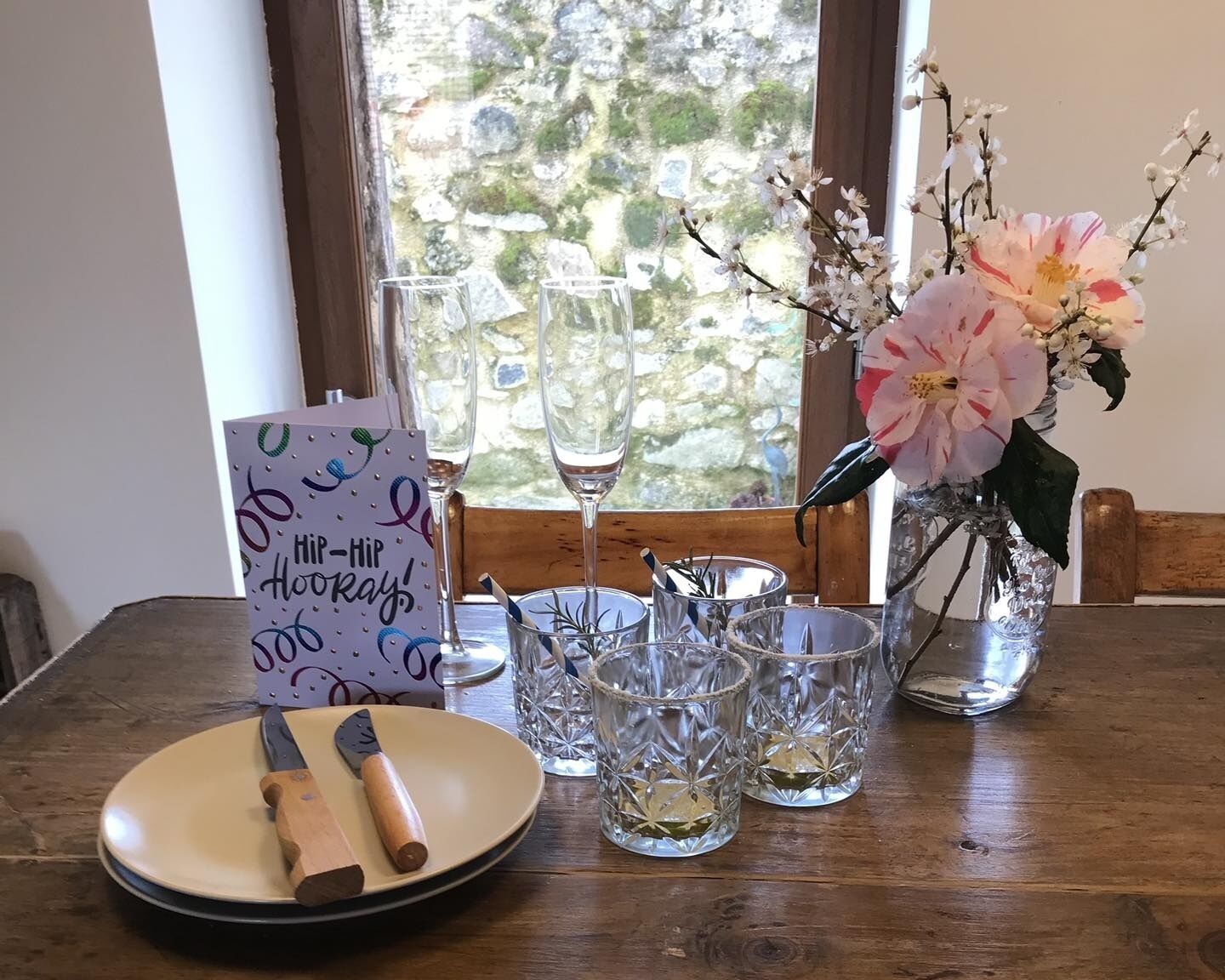 Une table dressée avec une assiette, un couteau et un verre contenant une boisson, ainsi qu’une carte et un vase rempli de fleurs.