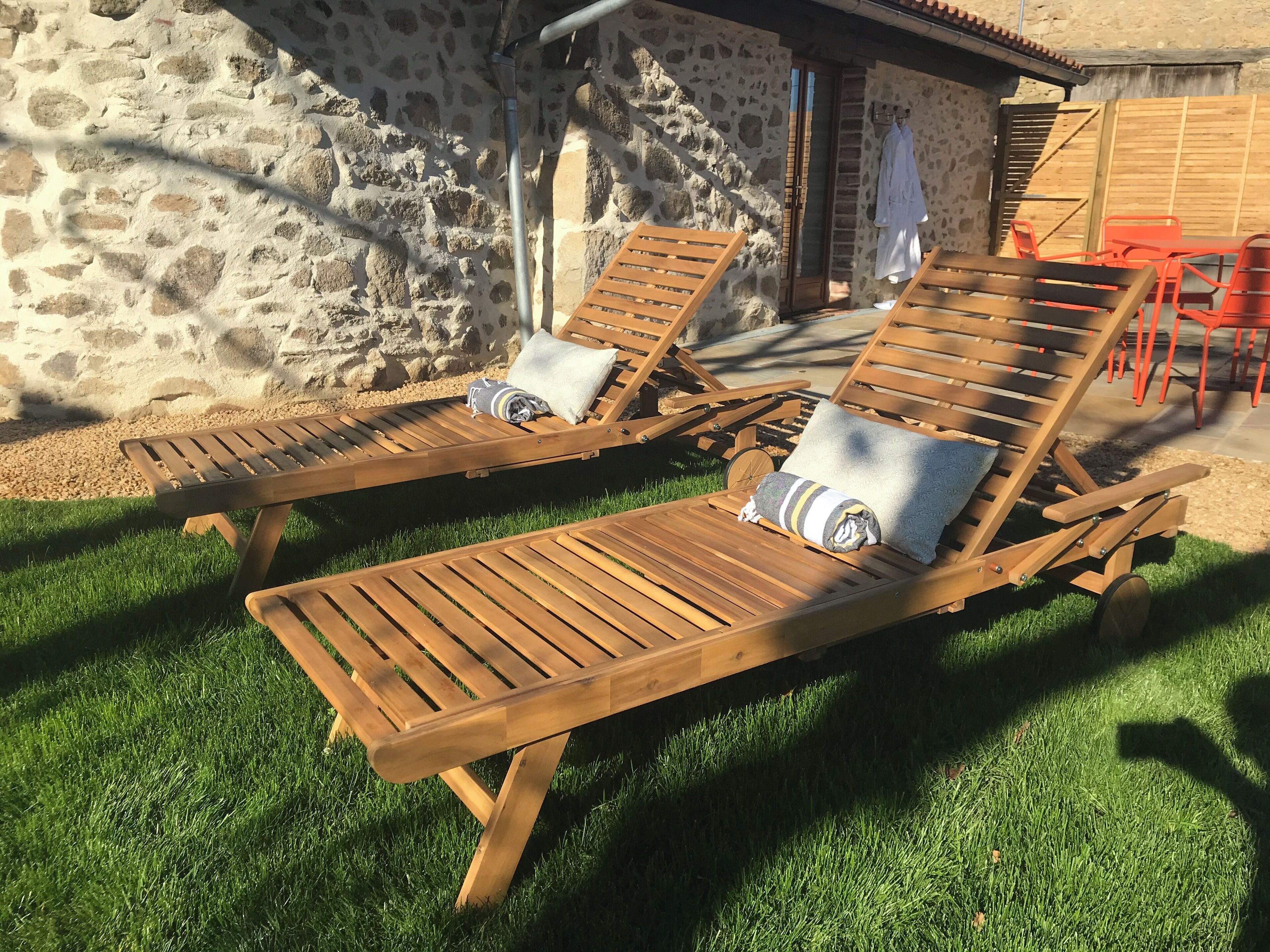 Zwei Holz-Loungesessel mit Kissen, eine Steinsäule und eine Holztür im Hintergrund.