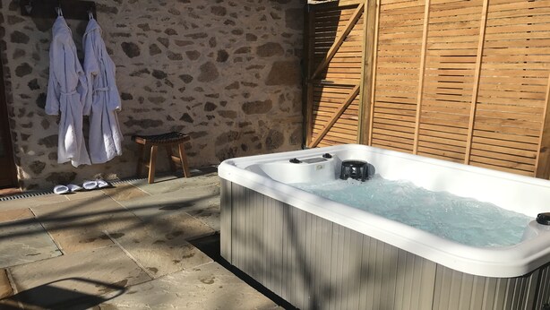 Un jacuzzi en un entorno exterior con paredes de piedra y listones de madera.