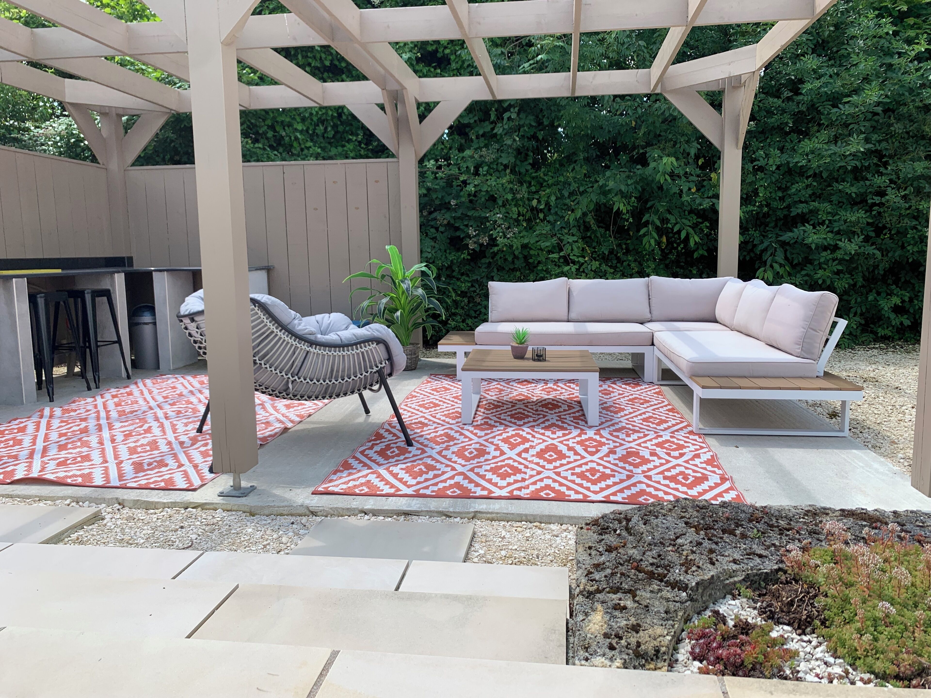 An outdoor patio with a white sofa, a wicker chair, a small table, and a patterned rug.