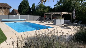 Un patio trasero con piscina, sillas de descanso, un pérgola y una zona de estar cubierta.