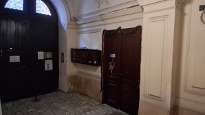Un corridoio con una porta in legno scuro, un muro bianco con un termostato e un pavimento piastrellato.