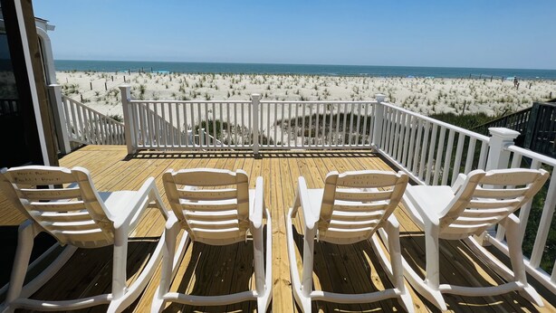 A deck with white chairs and a railing overlooking a beach. - 4BR 2BA OCEANFRONT COTTAGE- Fish, Fun & Sun! Relax, Recharge, Repeat!- Book Now! (Oak Island)