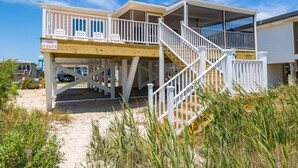 A beachfront house with a wooden deck, a covered porch, and a staircase leading to the upper level. - 4BR 2BA OCEANFRONT COTTAGE- Fish, Fun & Sun! Relax, Recharge, Repeat!- Book Now! (Oak Island)