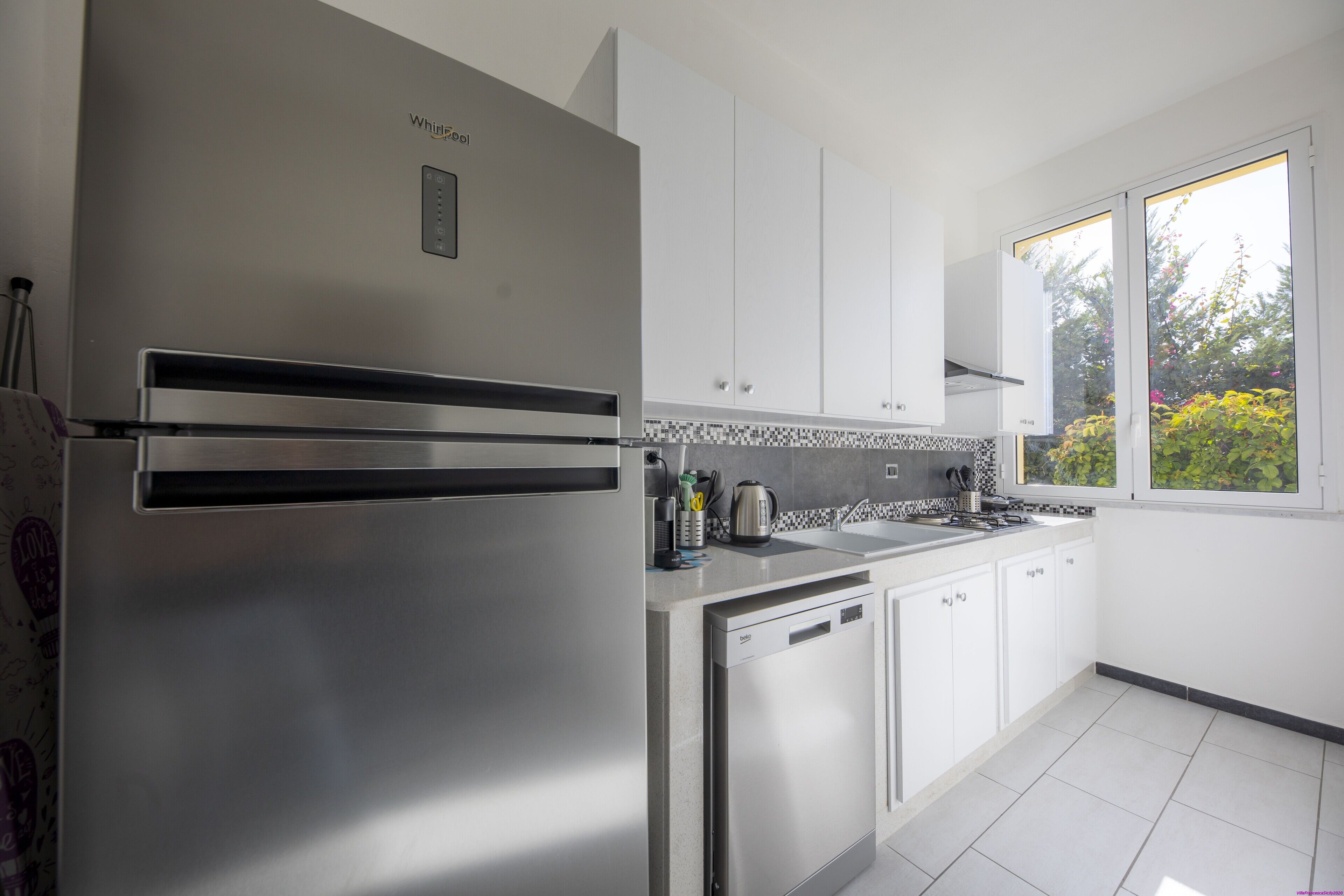 A modern kitchen with stainless steel appliances, white cabinets, and a window providing natural light.