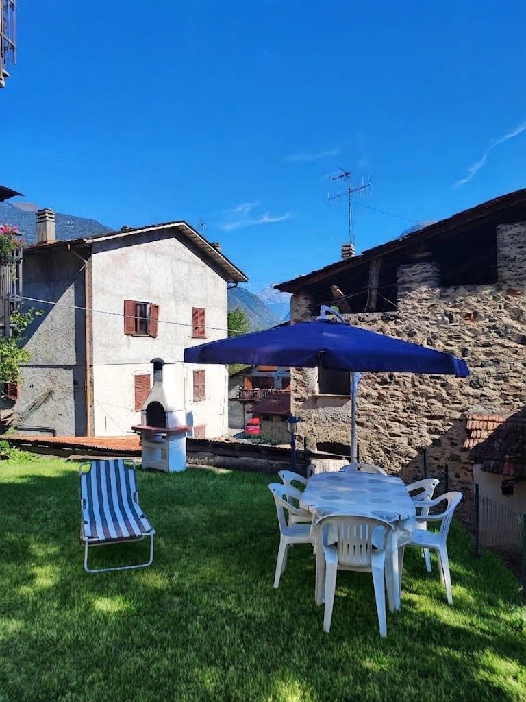 Eine Terrasse mit Tisch, Stühlen, einem blauen Sonnenschirm und einem Grill.