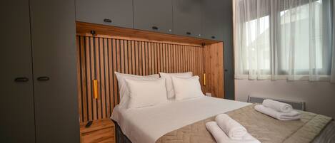A modern bedroom with a wooden headboard, a large bed with a beige quilt, and a bedside table with a remote control.