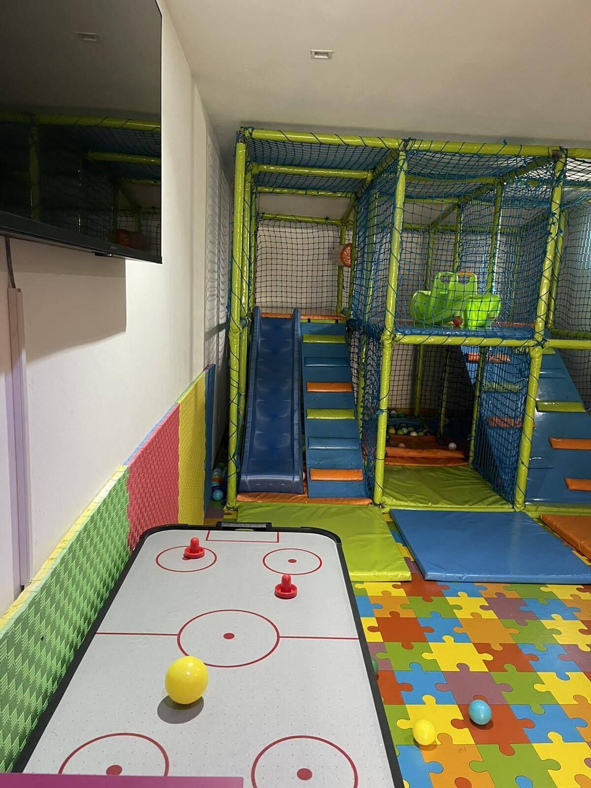 A play area with a shuffleboard table, slides, and a netted play structure.