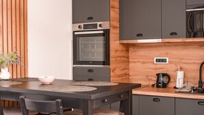 Une cuisine moderne avec des meubles de couleur sombre, un plafond en bois et un coin repas comprenant une table et des chaises.